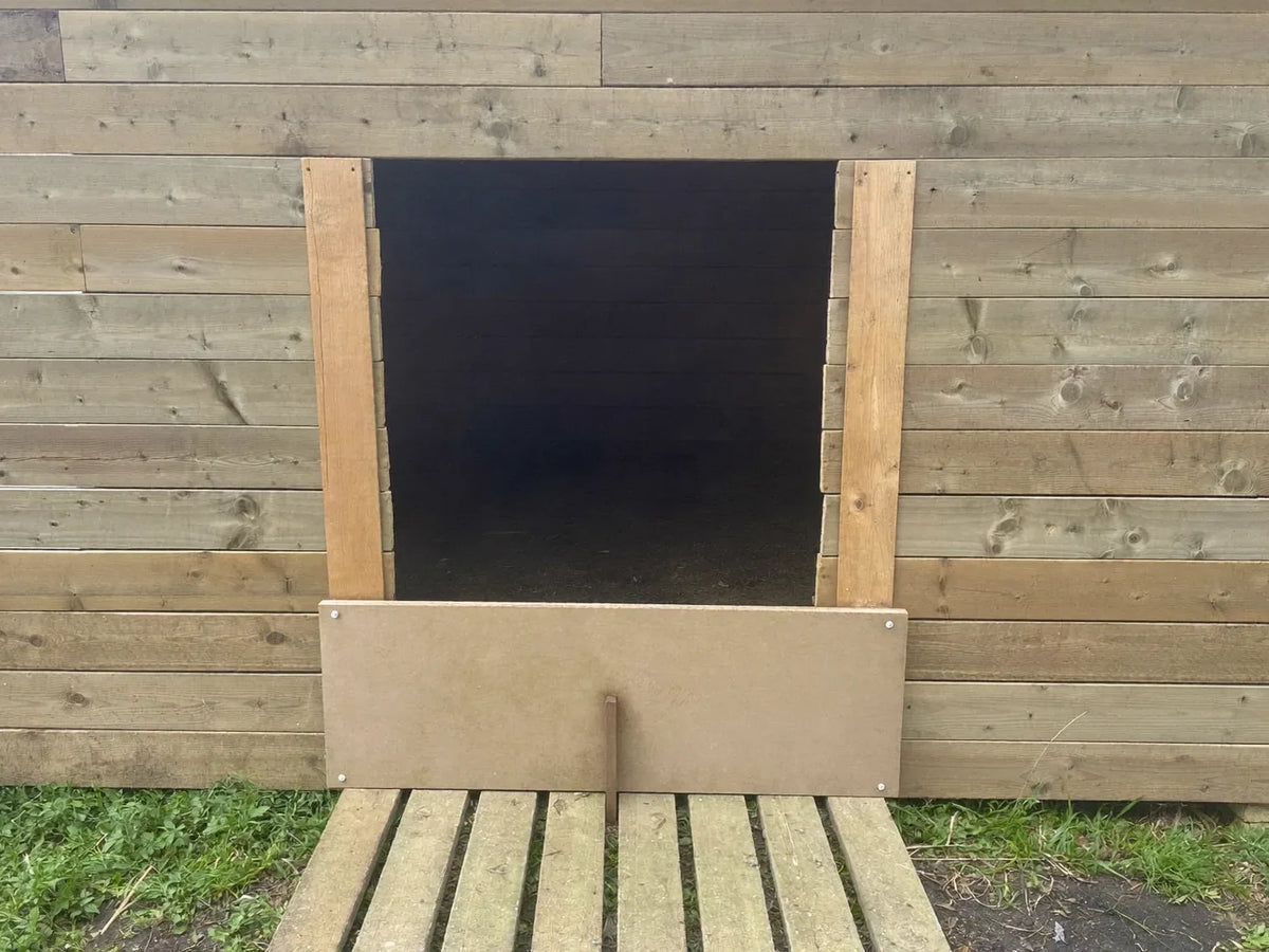Small hen-sized pop-hole cut into the timber wall of a backyard chicken coop, sliding panel raised in its runners