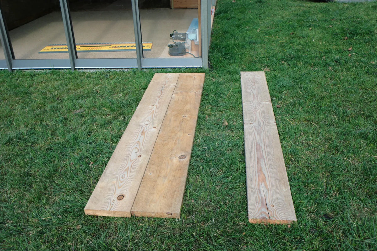 Spirit level and a timber pad beside the corner leg of a coop frame on mown grass