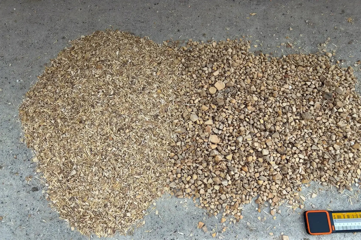 Loose chopped wheat straw heaped beside coarse softwood chips on a swept concrete floor, every piece separate