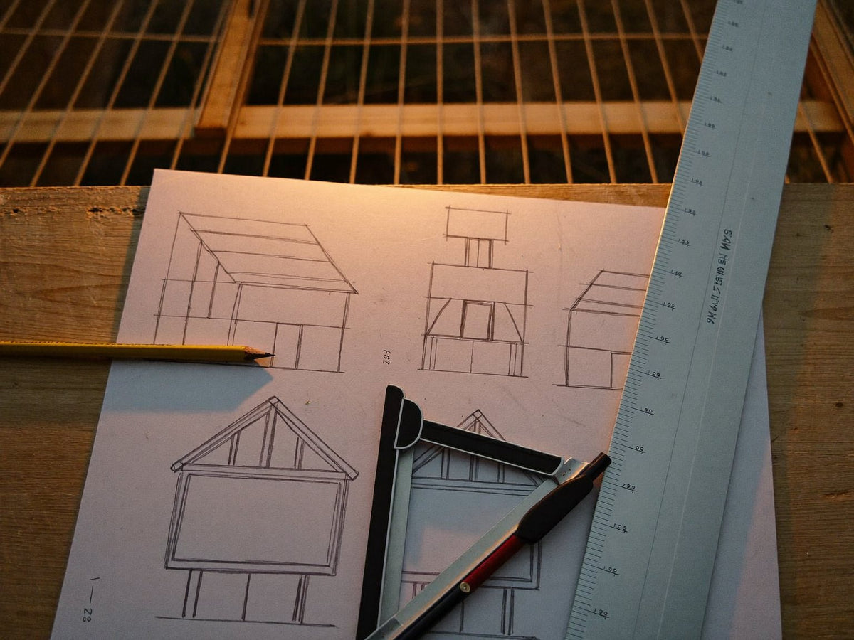 Pencil sketches of chicken coop elevations with a ruler and square on a work table
