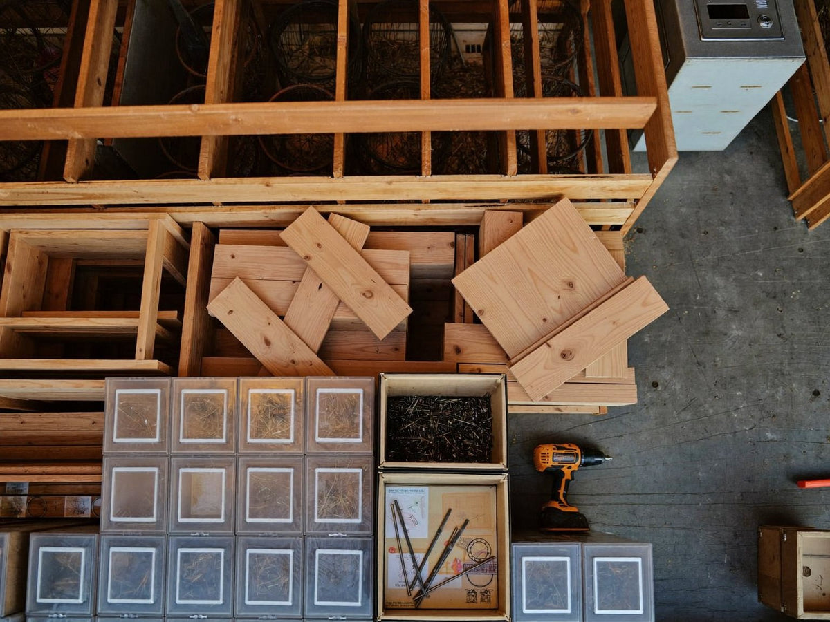 Overhead of a workshop bench with lumber offcuts, parts bins and a cordless drill