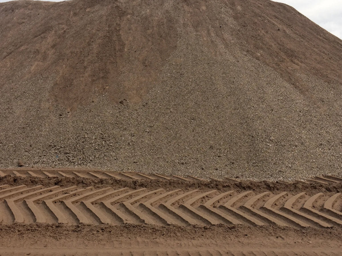 Heaped stockpile of loose damp washed sand in an aggregate yard with loader tyre tracks across the ground