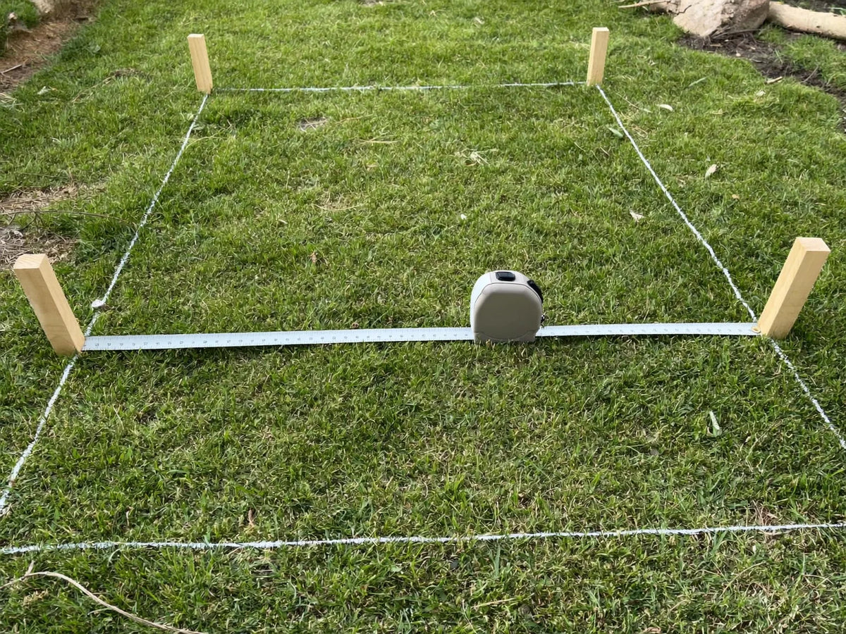 Tape measure stretched across a mown grass rectangle marked out for a chicken coop
