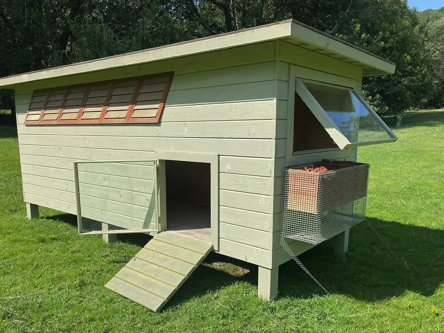 Open side window and louvered upper vents on a wooden chicken coop in bright summer light