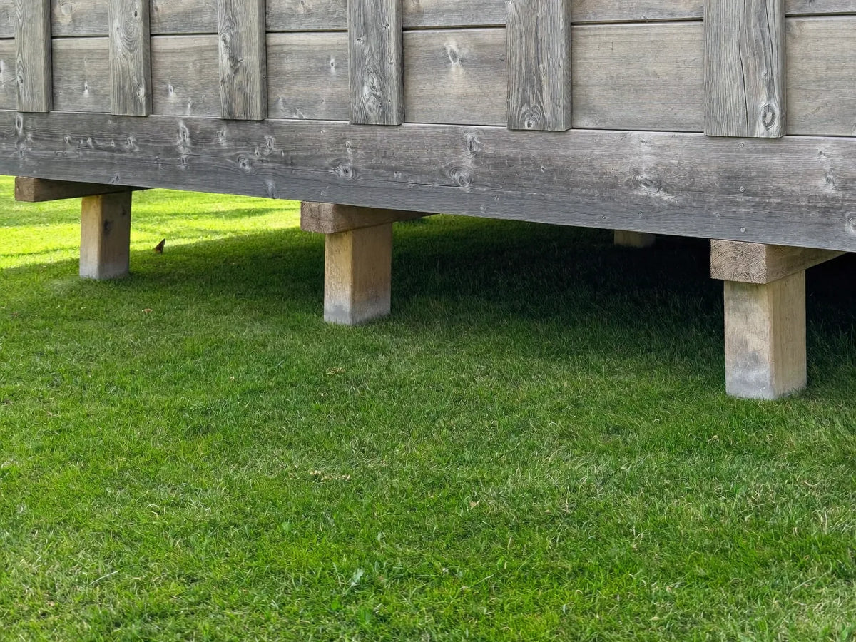 Bottom rail and legs of a wooden chicken coop with daylight showing in the gap above mown grass