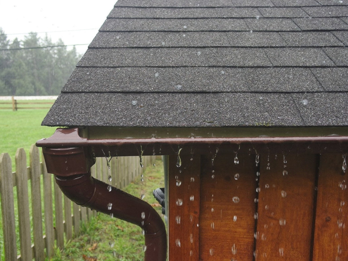 Rain running off the shingled roof and overhanging eave of a wooden chicken coop