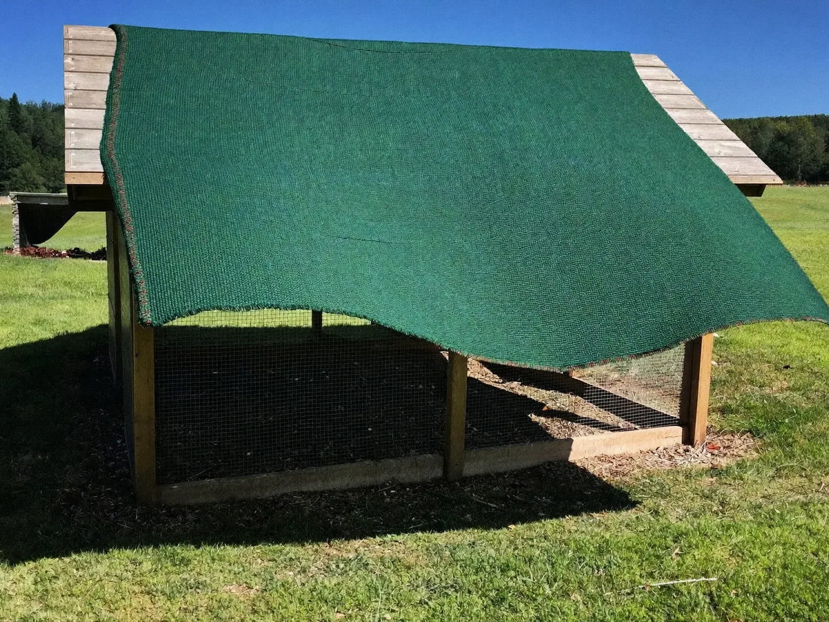 Knitted shade fabric sloped over the mesh run of a small wooden backyard chicken coop in high summer sun