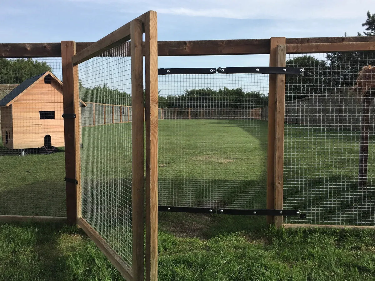 Wire-mesh gate in the side of a chicken run beside a wheeled wooden coop on mown grass