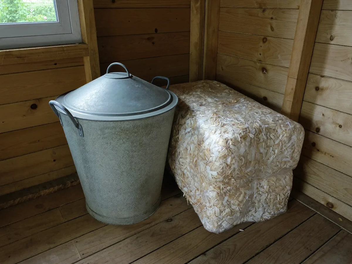 Lidded metal feed can standing in a dry corner beside a bale of bedding