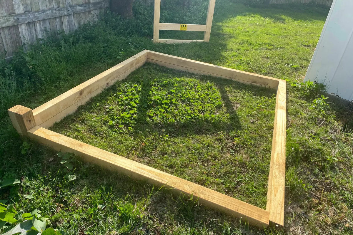 Squared timber floor frame for a small coop on mown grass with one wall frame raised behind it