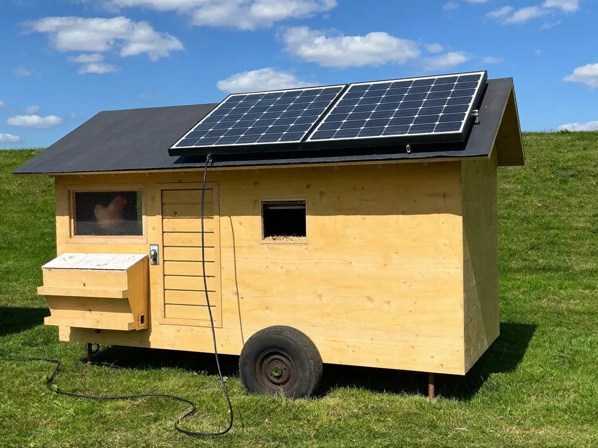 Small solar panel lying flat on the sunlit roof of a wheeled wooden chicken coop on a mown lawn